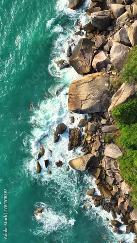 Ocean waves crashing on rocks. Top aerial drone view of waves crashing on rocky coastline. Blue ocean. Aerial vertical, vertical video background.