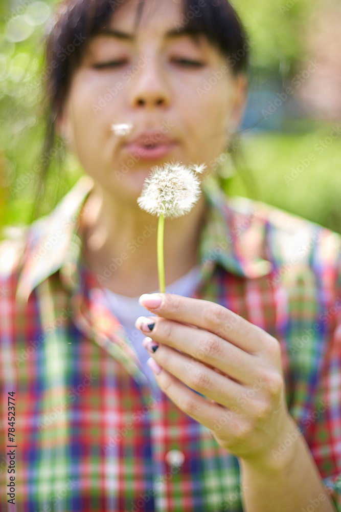 Woman Blowing Dandelion Seeds in a Sunny Garden During Springtime Woman Blowing Dandelion Seeds in a Sunny Garden During Springtime