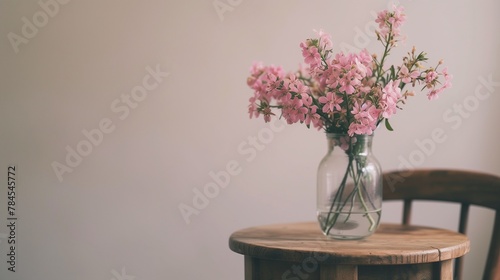 Cute pink flowers in glass vase placed on wooden table standing by small chair