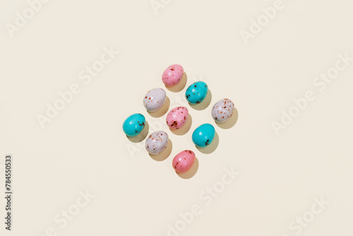 Pattern of chocolate Easter eggs in pink, beige and blue colors on a beige background. Creative Easter concept