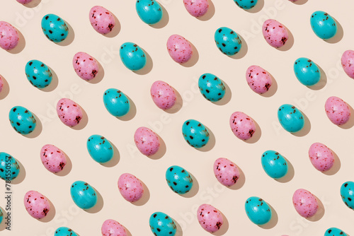 Pattern of chocolate Easter eggs in pink and blue colors on a beige background. Creative Easter concept