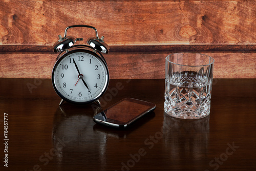 Alarm Clock with Mobile Phone and Glass of Water on a Bedside Shelf