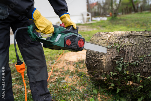 Photos A man in uniform cuts an old tree in the yard with an electric saw