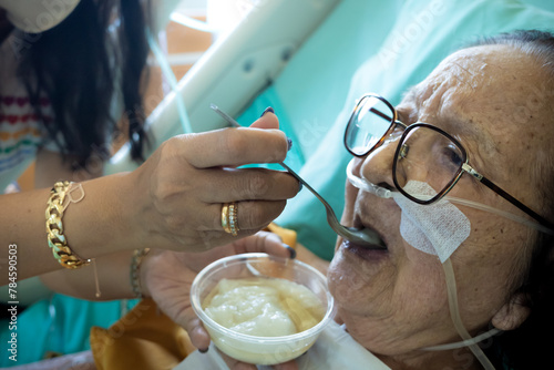 A daughter feeding delicate food to her sick elderly mother in a hospital bed