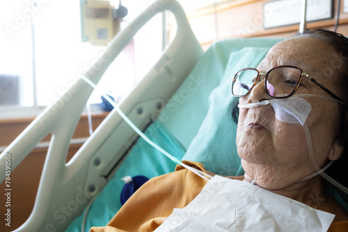 Sick Asian elderly woman lying in hospital bed undergoing inpatient treatment wearing oxygen tube