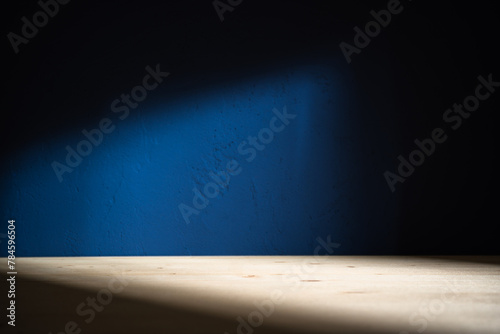 Table on dark blue wall background. Minimalist composition with abstract shadow on the wall and light reflections. Mock up for presentation, branding products, cosmetics food or jewelry.	