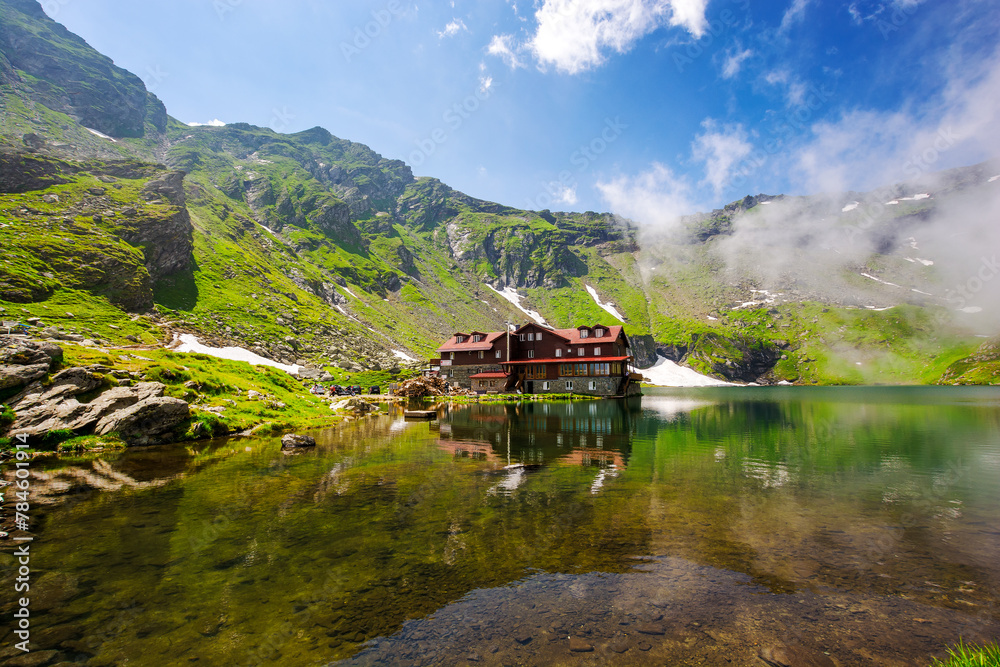 Fototapeta premium alpine landscape of fagaras mountains. balea lake of romania in summer. sunny weather with clouds on the blue sky. spots of snow and grass on the rocky hillside. scenery reflecting in the water