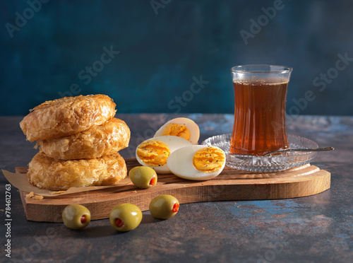 Turkish Traditional Bakery Item (Boyoz) with boiled egg, olives and hot tea in a clear glass; blue background; copy space