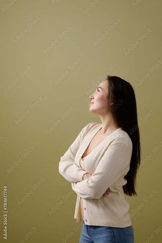Profile of dreamy asian woman in cardigan looking away isolated on green Profile of dreamy asian woman in cardigan looking away isolated on green
