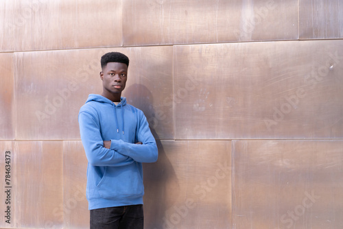A young man in a blue hoodie stands in front of a wall