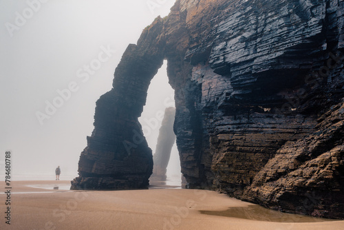 Tourist walking along natural arch on Cathedrals beach in Galicia, Spainn. Man silhouette in foggy landscape with Playa de Las Catedrales Catedrais beach in Ribadeo, Lugo on Cantabrian coast photo