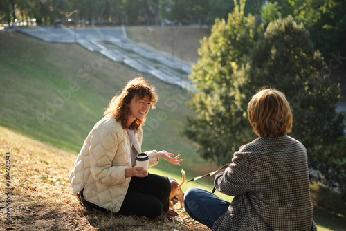 Wallpaper Mural Two friends talking and laughing sitting on the grass in a park. Drinking coffee to go, with small dog in the sweater. Sunny evening light, weekend concept. High quality photo Torontodigital.ca