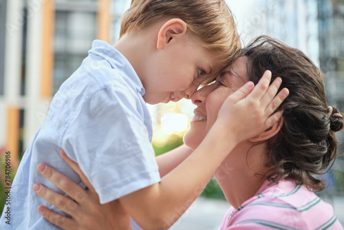 Adorable mother and son smiling happy having fun at city background. Motherhood concept, hugging. Boy 8 years old with mother in bright clothes enjoying summer day. High quality photo