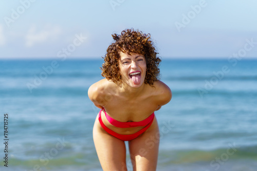 Happy woman standing near seawater and showing tongue