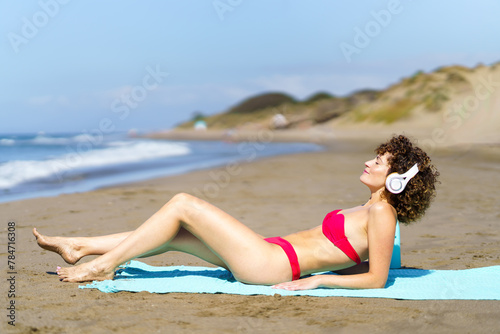 Content woman in headphones chilling on beach