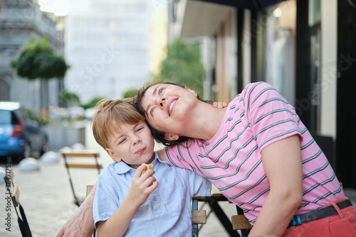 Young mother and her son having sweets in outdoor restaurant on summer day. Sitting together, hugging and laughing, enjoying weekend. High quality photo