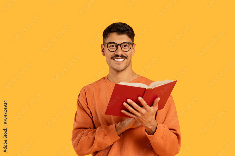 Smiling man with glasses reading a red book Smiling man with glasses reading a red book