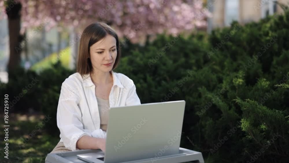Digital Nomad, Woman Working, Sakura Sunshine. Encircled by blossoming sakura trees, woman is focused on her laptop work in park. Digital Nomad, Woman Working, Sakura Sunshine. Encircled by blossoming sakura trees, woman is focused on her laptop work in park.