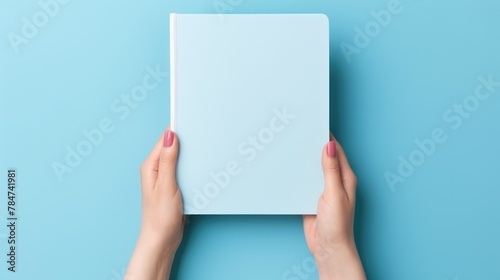 A clean notebook for notes is held by women's hands on a colored background, concepts of education, workplace, creativity. A place for text or advertising. © Cherkasova Alie