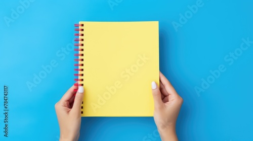 A clean notebook for notes is held by women's hands on a colored background, concepts of education, workplace, creativity. A place for text or advertising. © Cherkasova Alie