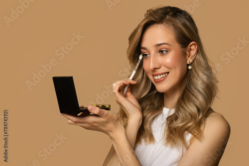Happy smiling woman applying makeup with brush. Beige background
