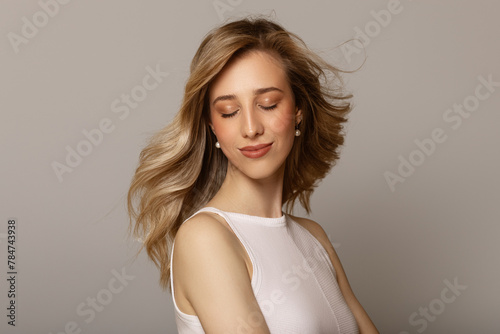 Portrait of a beautiful young woman. Hair blowing in the wind. Wavy hair and makeup. Gray background