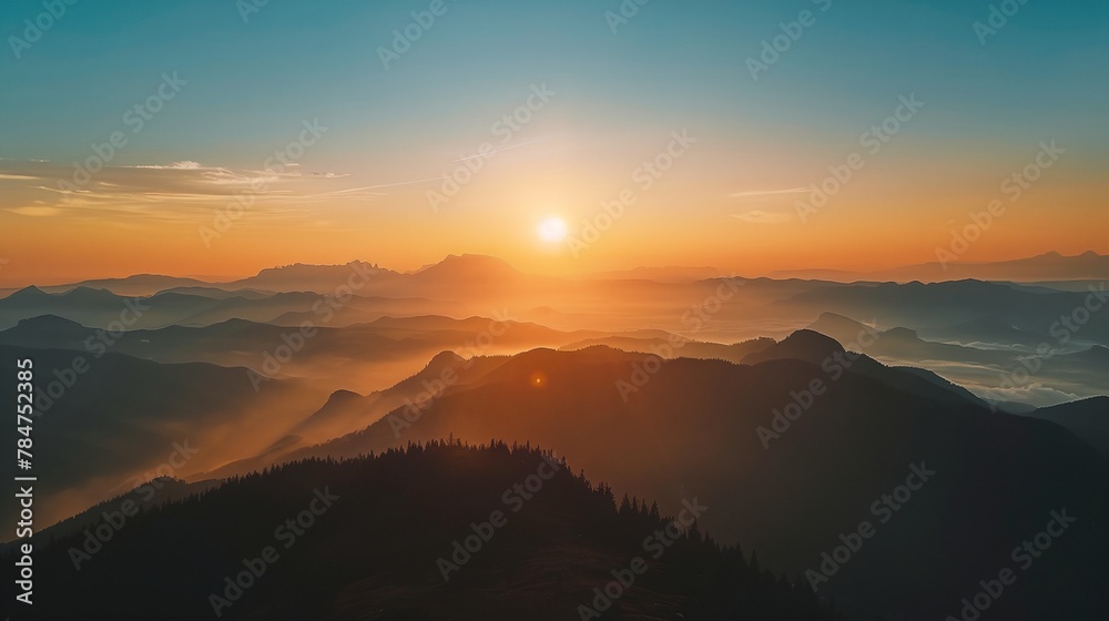 a sunset over a mountain range with a bright orange sun in the distance and a hazy sky above it