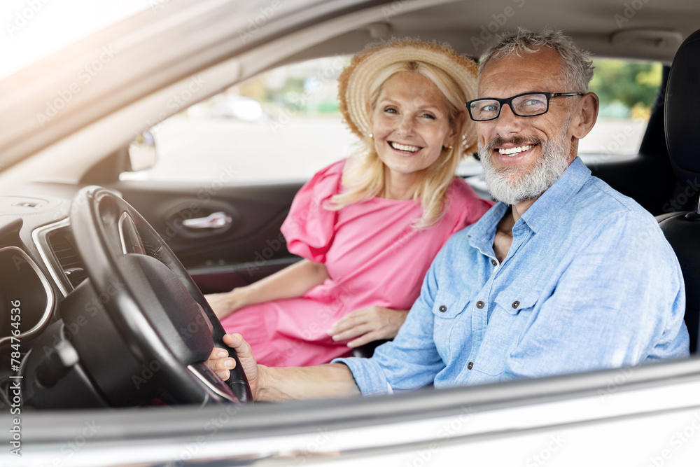 Happy elderly couple in car with window down - obrazy, fototapety, plakaty 