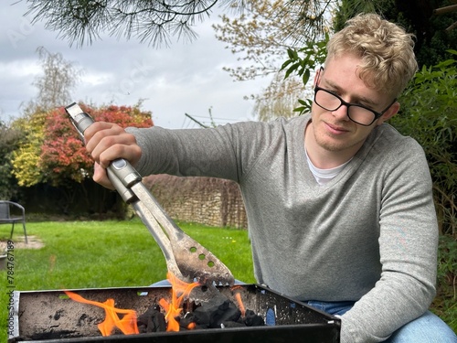 Young man starting barbecue grill flame, having bbq party in his backyard