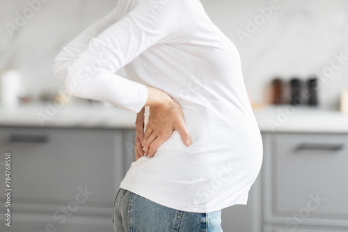 Pregnant woman touches her back gently, cropped photo
