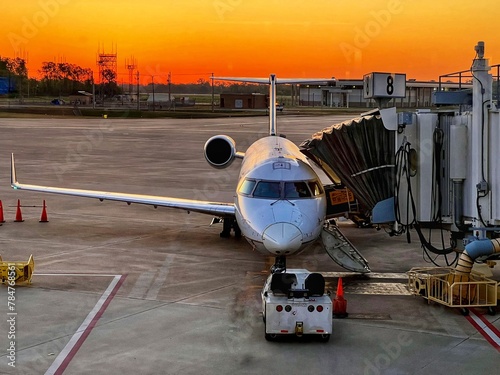 Small jet at an airport terminal attached to a sky bridge with an orange sky background