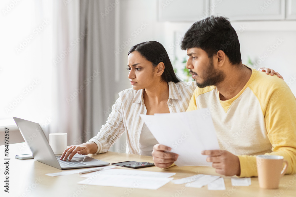 Serious Indian couple discussing finances online, kitchen interior Serious Indian couple discussing finances online, kitchen interior