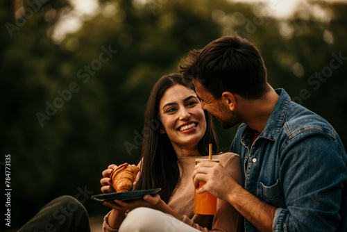 Diverse couple laughing and enjoying snacks and fresh juice during a picnic outing
