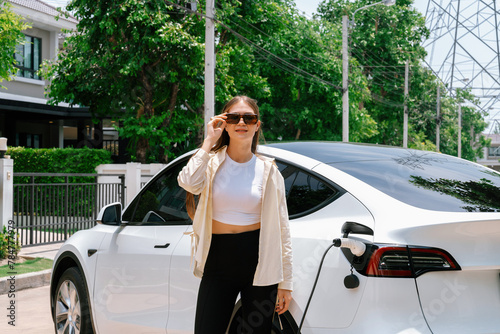 Eco-friendly conscious woman recharging EV vehicle from home charging station. EV electric car technology utilized as alternative transportation for future sustainability. Expedient photo