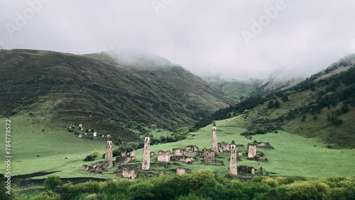 View of the medieval Targim tower complex in the Caucasus mountains surrounded by greenery. The Caucasus Mountains on a cloudy day in Ingushetia. Russia, 4K. photo