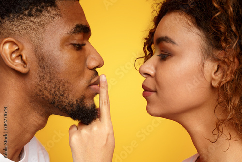 Profile of mysterious woman touching male lips with finger