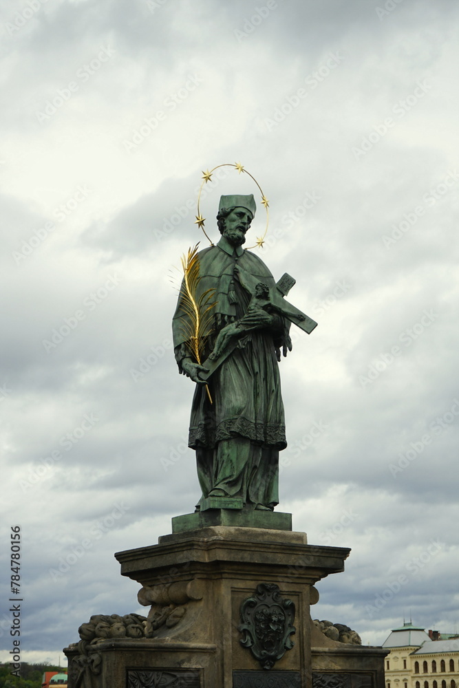 Obraz premium Der Heilige Johannes Nepomuk als Statue und Denkmal vor dunklem Himmel mit Regenwolken auf der Karlsbrücke über die Moldau in der Altstadt von Prag in Tschechien