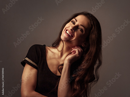 Toothy smiling beautiful woman with brown long hair looking on dark shadow background with empty copy space. Closeup