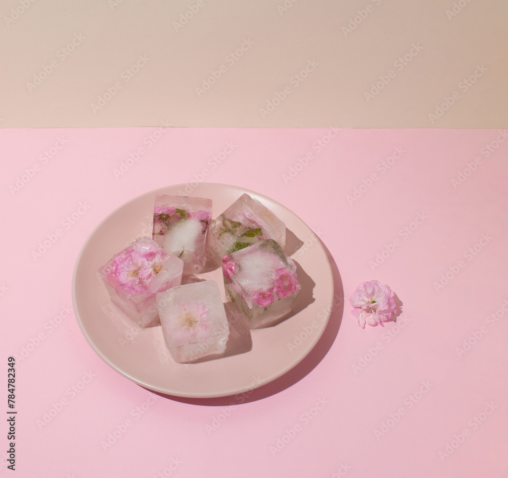 Beautiful small pink flowers in ice cubes on pink plate on beige background, top view Beautiful small pink flowers in ice cubes on pink plate on beige background, top view