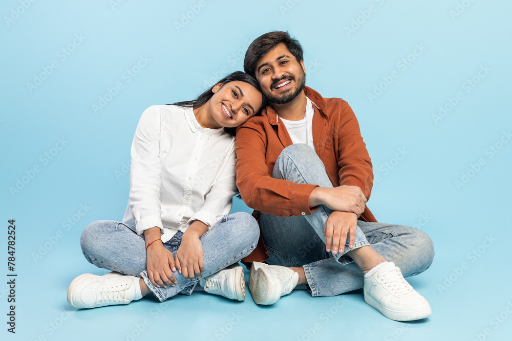 Smiling couple sitting together on floor on blue background Smiling couple sitting together on floor on blue background
