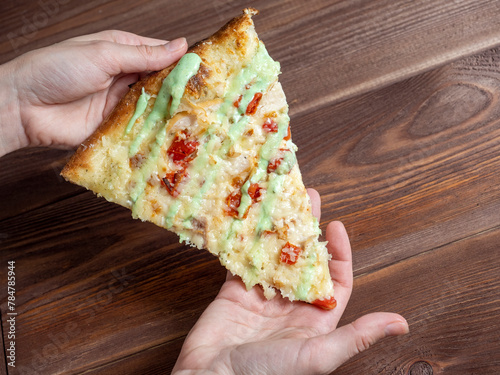 hands holding one piece of pizza on a wooden table