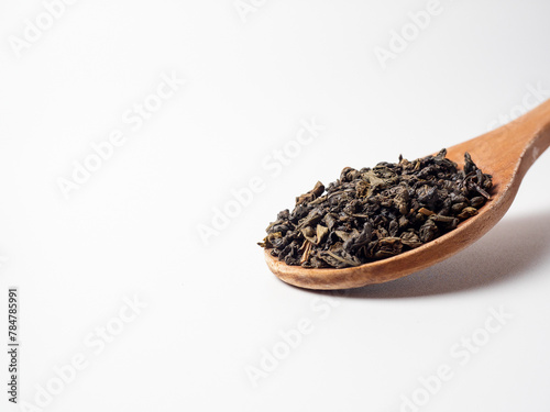 dry black tea leaves in a wooden spoon on a white background. Healthy tonic drink
