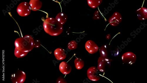 Delicious juicy red cherries are bouncing up and rotating on a black background in slow motion