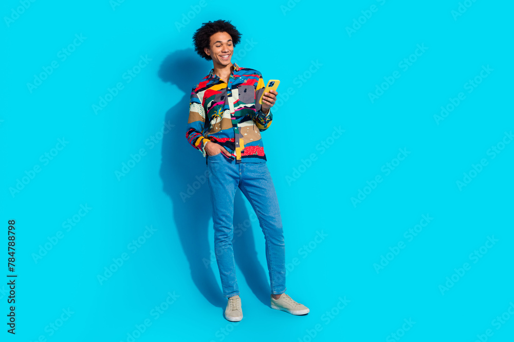 Full size photo of handsome young guy hold telephone dressed stylish print garment isolated on blue color background Full size photo of handsome young guy hold telephone dressed stylish print garment isolated on blue color background