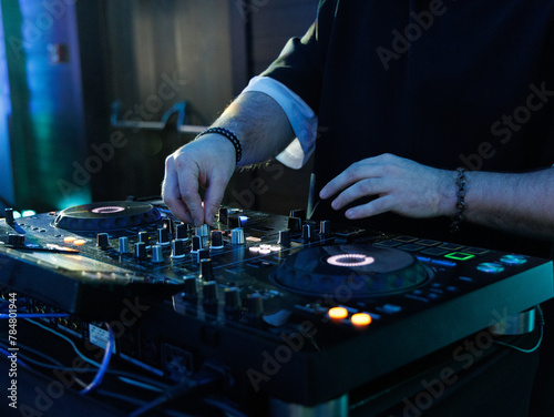 DJ plays live set and mixing music on turntable console at stage in the night club. Disc Jokey Hands on a sound mixer station at club party