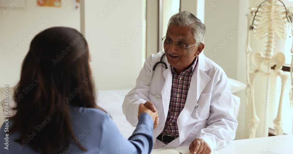 Serious old doctor man discussing successful treatment, therapy success with younger female patient, shaking hands, getting happy, smiling, laughing. Woman thanking senior practitioner Serious old doctor man discussing successful treatment, therapy success with younger female patient, shaking hands, getting happy, smiling, laughing. Woman thanking senior practitioner