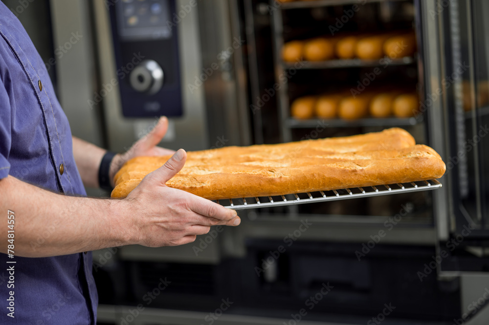 Baker putting tray with baguettes to oven at commercial bakery - obrazy, fototapety, plakaty 