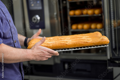 Baker putting tray with baguettes to oven at commercial bakery