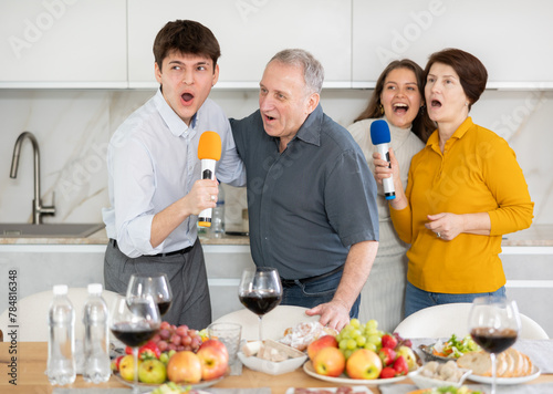 Party and karaoke at house for fun social event or gathering together in celebration. Happy family singing song using microphone at festive table at home
