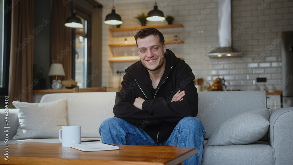 Handsome folded arms young man sitting on the sofa looking at camera and smiling at home. Handsome folded arms young man sitting on the sofa looking at camera and smiling at home.